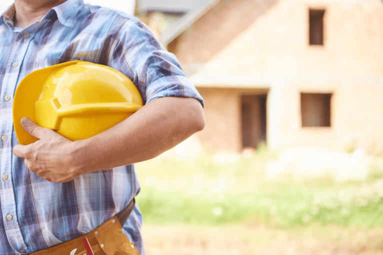 Construction worker holding yellow hard hat at building site