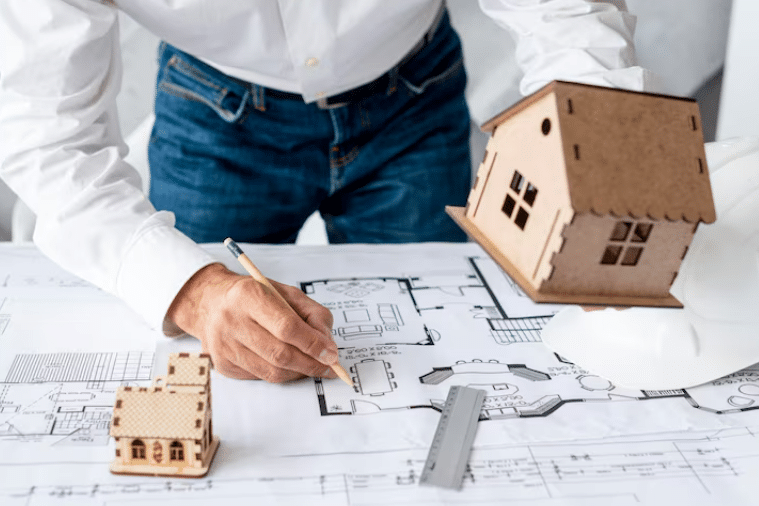 Architect drawing house plans with miniature house models