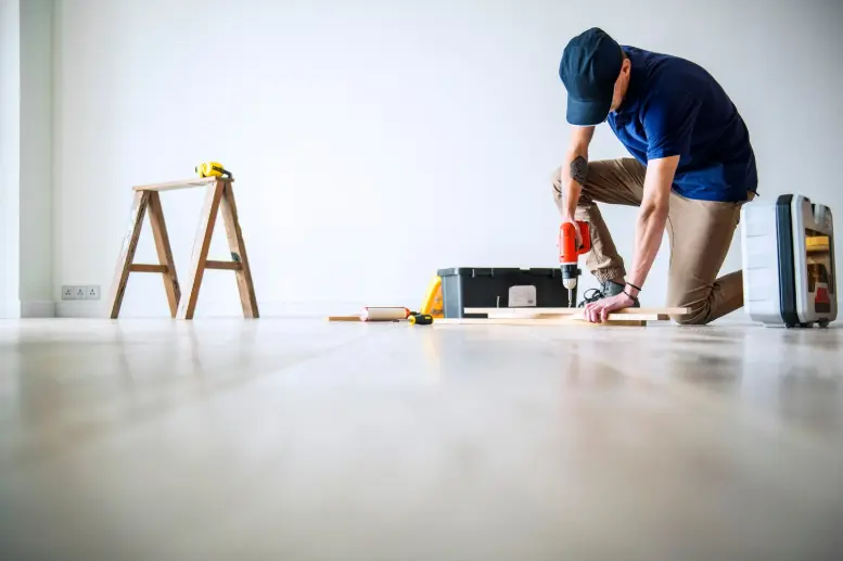 Contractor installing flooring with a power drill in a newly renovated residential interior.