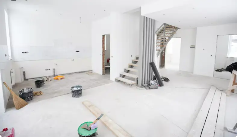 Open-concept home interior undergoing renovation with unfinished flooring, staircase, and construction materials.