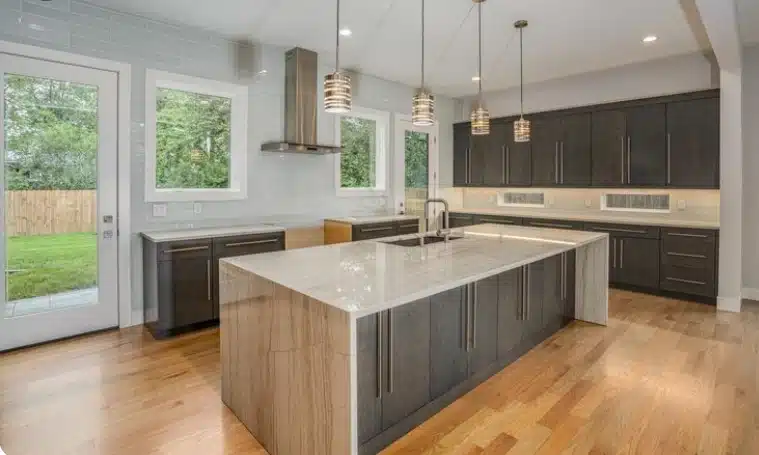 Modern open-concept kitchen with white cabinetry, quartz island, hardwood flooring, and large windows.