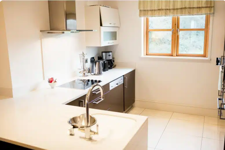 Bright modern kitchen with white countertops, sleek cabinetry, large windows, and stainless steel fixtures.
