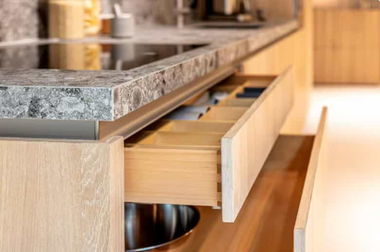Custom wood kitchen drawer organizer beneath a stone countertop with built-in storage compartments.