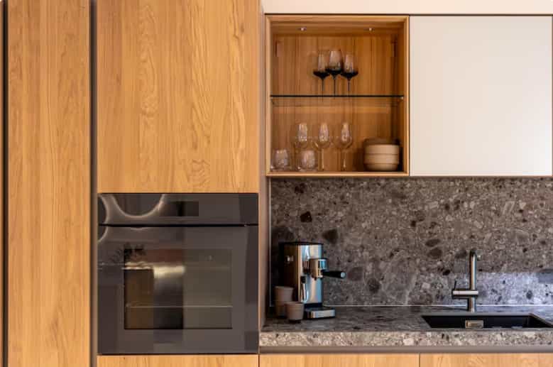 Custom wood kitchen cabinetry with built-in oven, stone backsplash, and modern storage solutions.